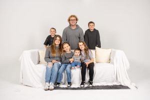A group sits together on a white covered couch against a light background in a studio setting.