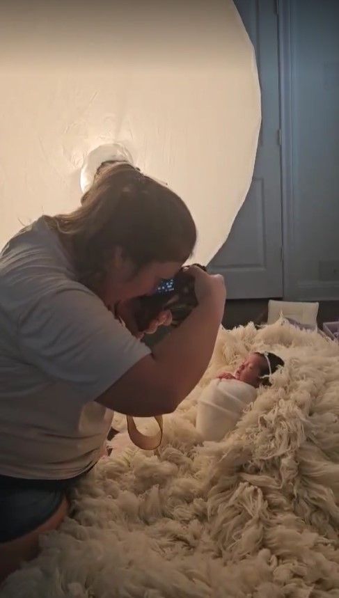 Behind the scenes of a newborn photo session with photographer working with fluffy white props.