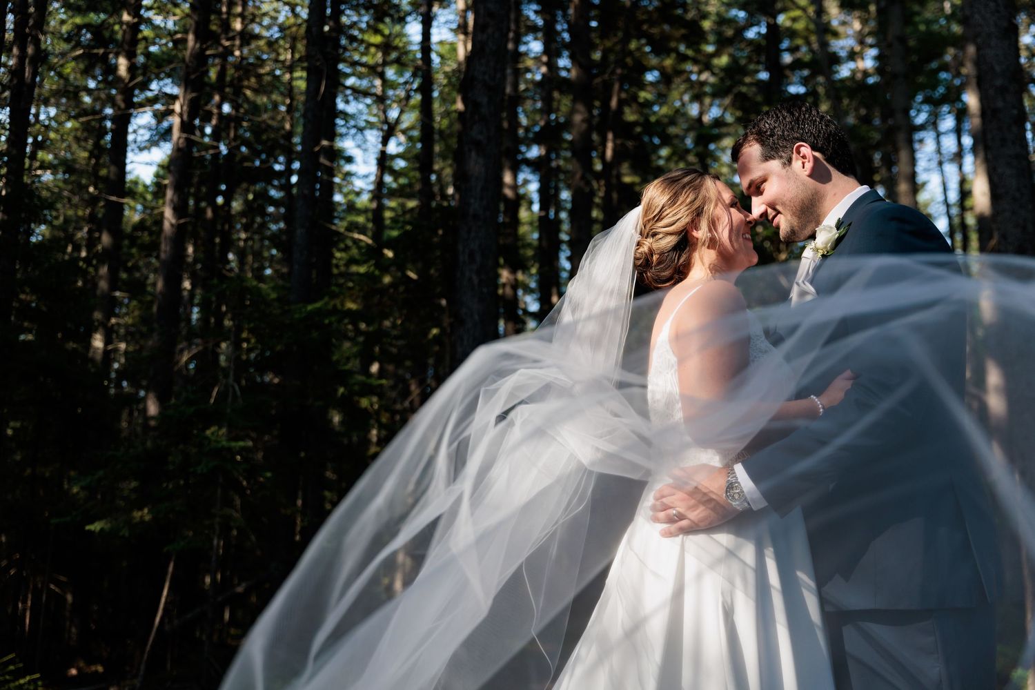 Ethereal wedding photography in a sunlit forest with flowing white dress details.