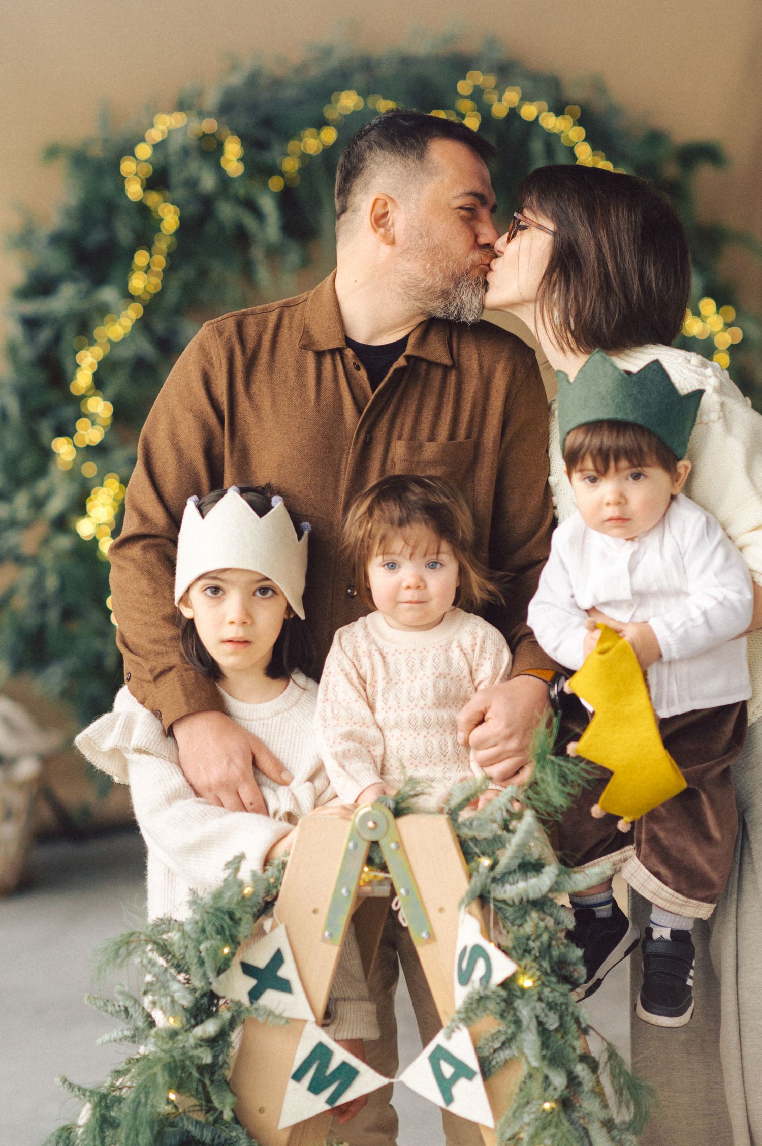 A family dressed in brown and white sits together holding holiday greenery and decorative yellow paper accents.