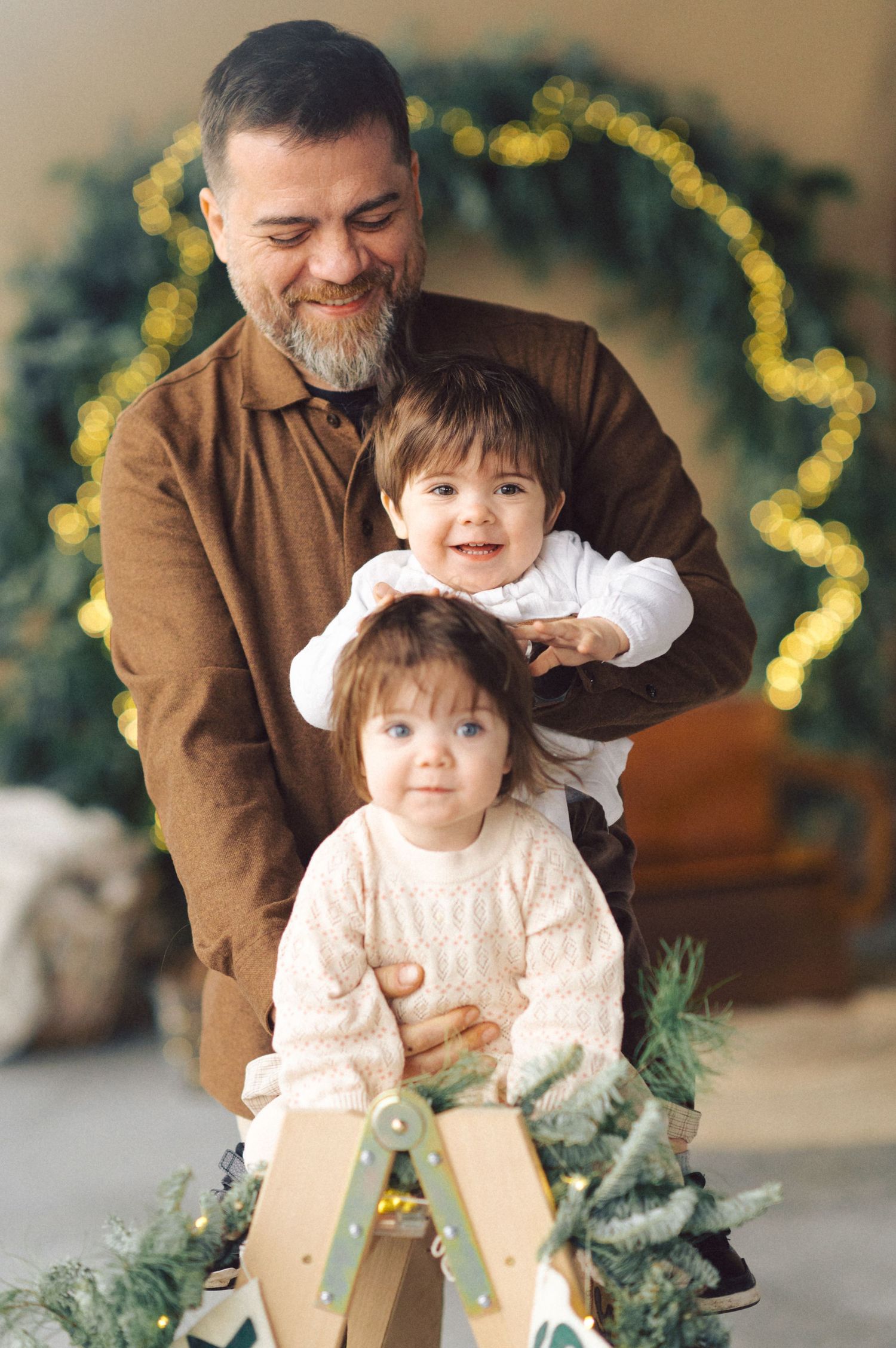 Family enjoying holiday season together with festive greenery and twinkling lights in background.