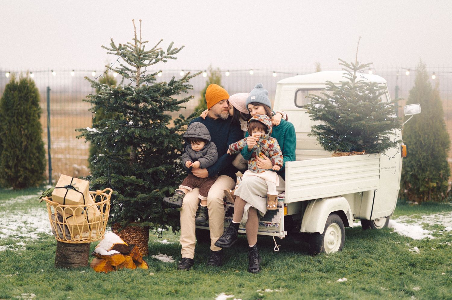 People sitting outdoors near Christmas trees during a snowy winter day at a seasonal tree lot.