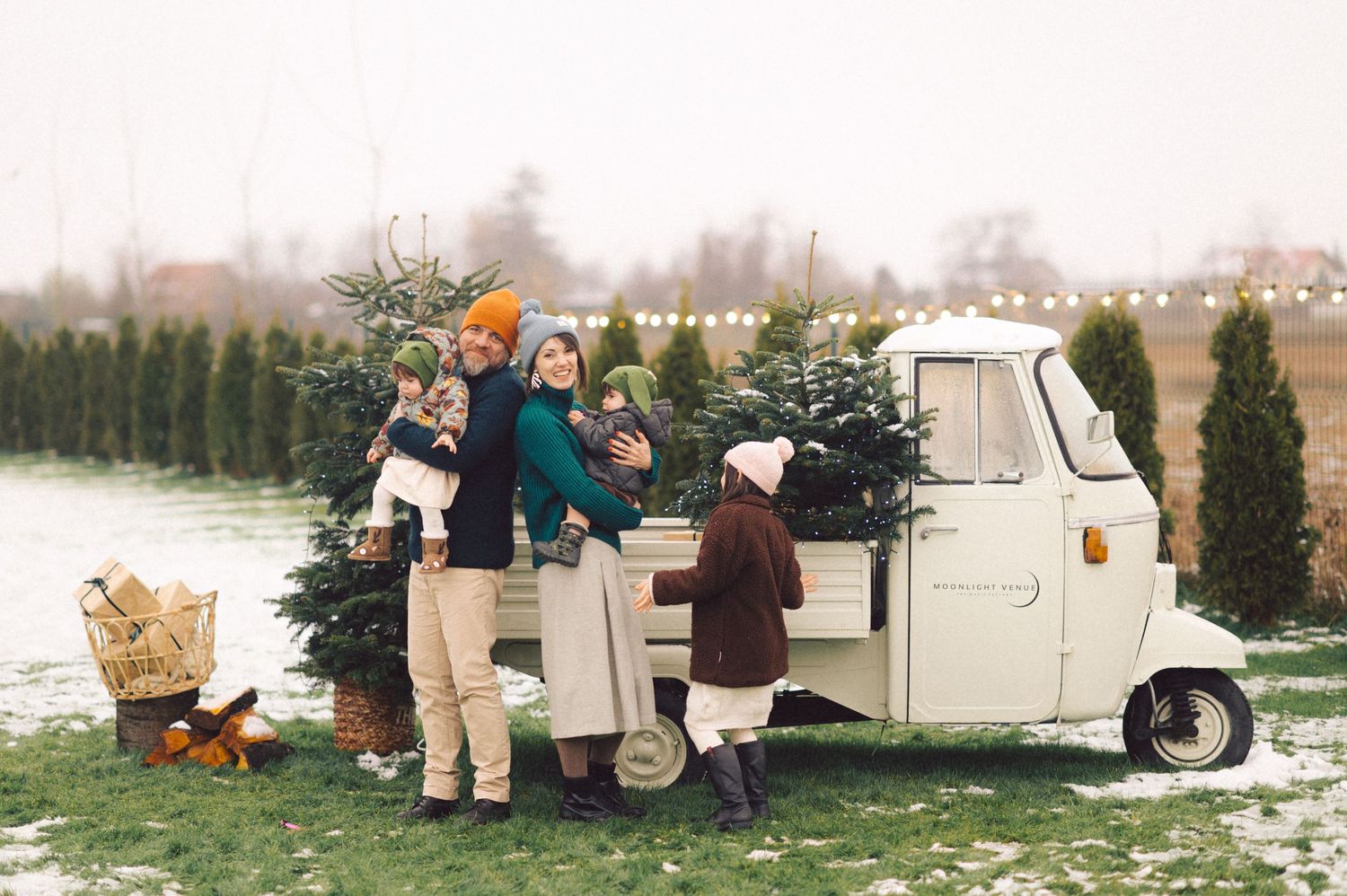 Couch setting in a snowy winter landscape with holiday decor and plaid blankets next to an RV camper.