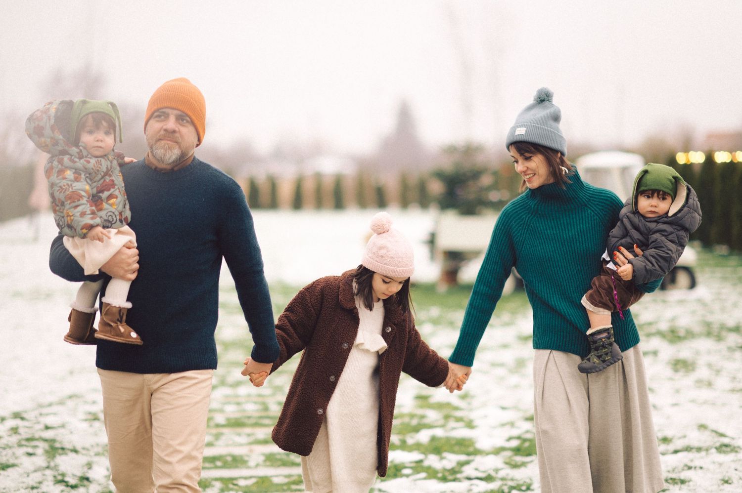 Family walking together and playing in the snow on a winter day, wearing warm coats and winter accessories.