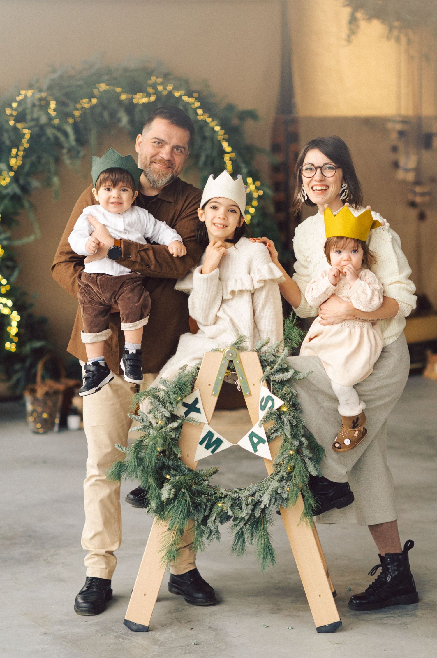 A family poses together for a holiday portrait with a decorative wooden letter A and evergreen wreath with twinkle lights.