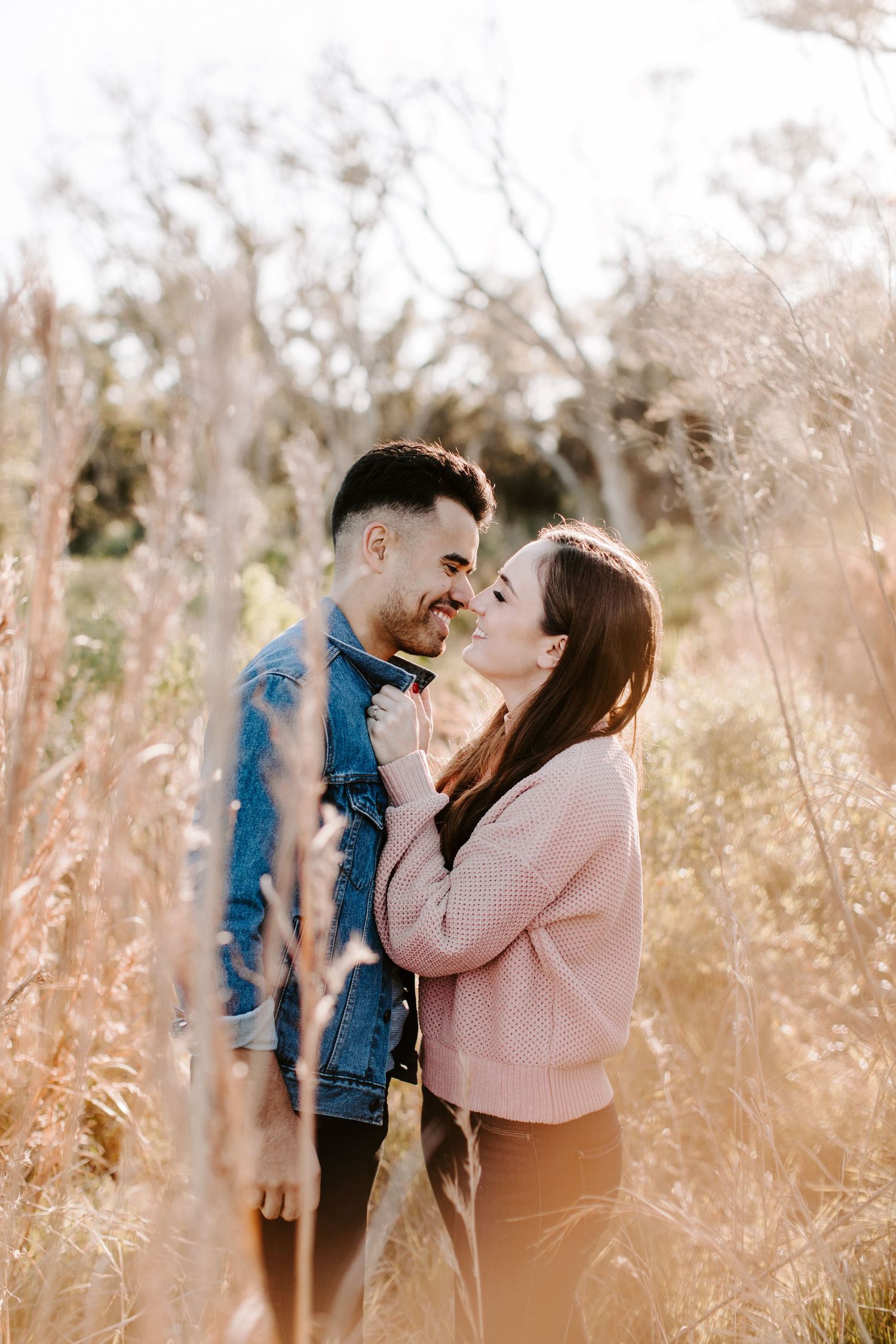 Romantic couple sharing tender moments in tall grasses during an outdoor photoshoot.