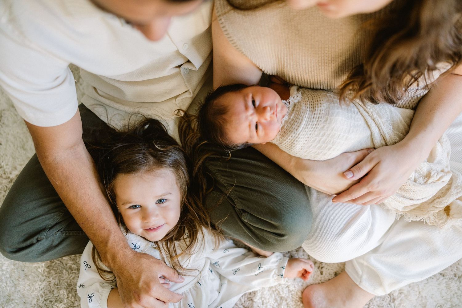 A series of intimate black and white lifestyle photos showing family members lying together in casual poses on light bedding.