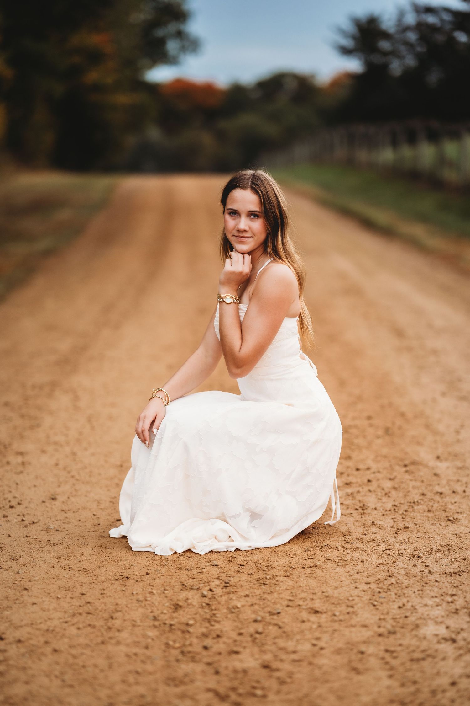 A person wearing a white dress sits thoughtfully in a summer field of tall grass at sunset.