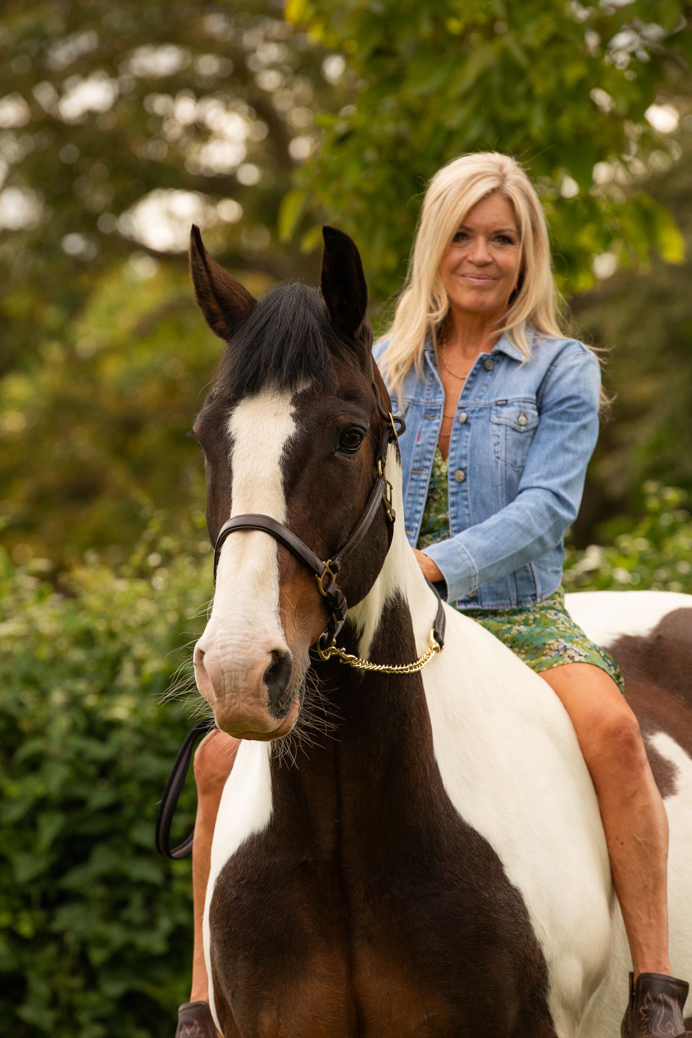 Young girl in denim overalls embraces a palomino horse in a sun-dappled forest setting.