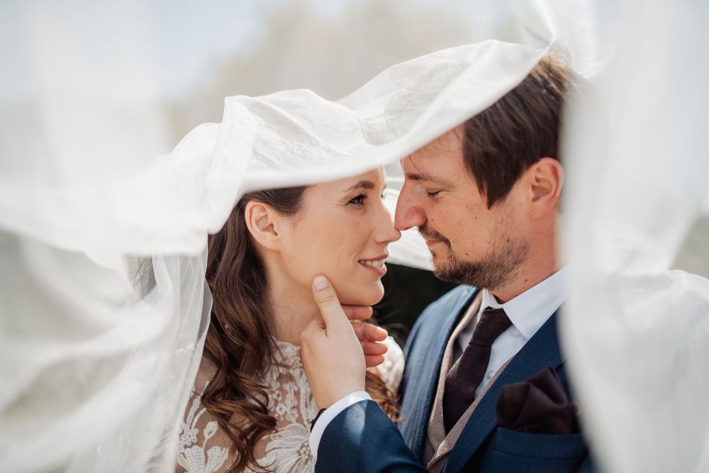 A romantic wedding moment captured under a flowing white veil as a couple shares an intimate close up.