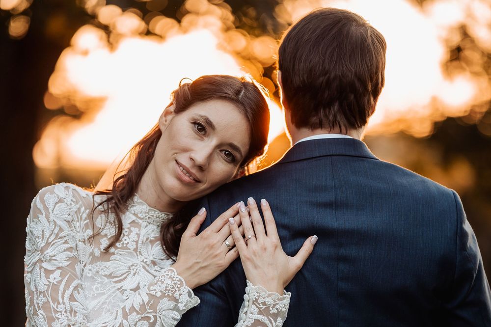Newlywed couple embraces during golden sunset with bride wearing lace long sleeve dress and groom in navy suit.