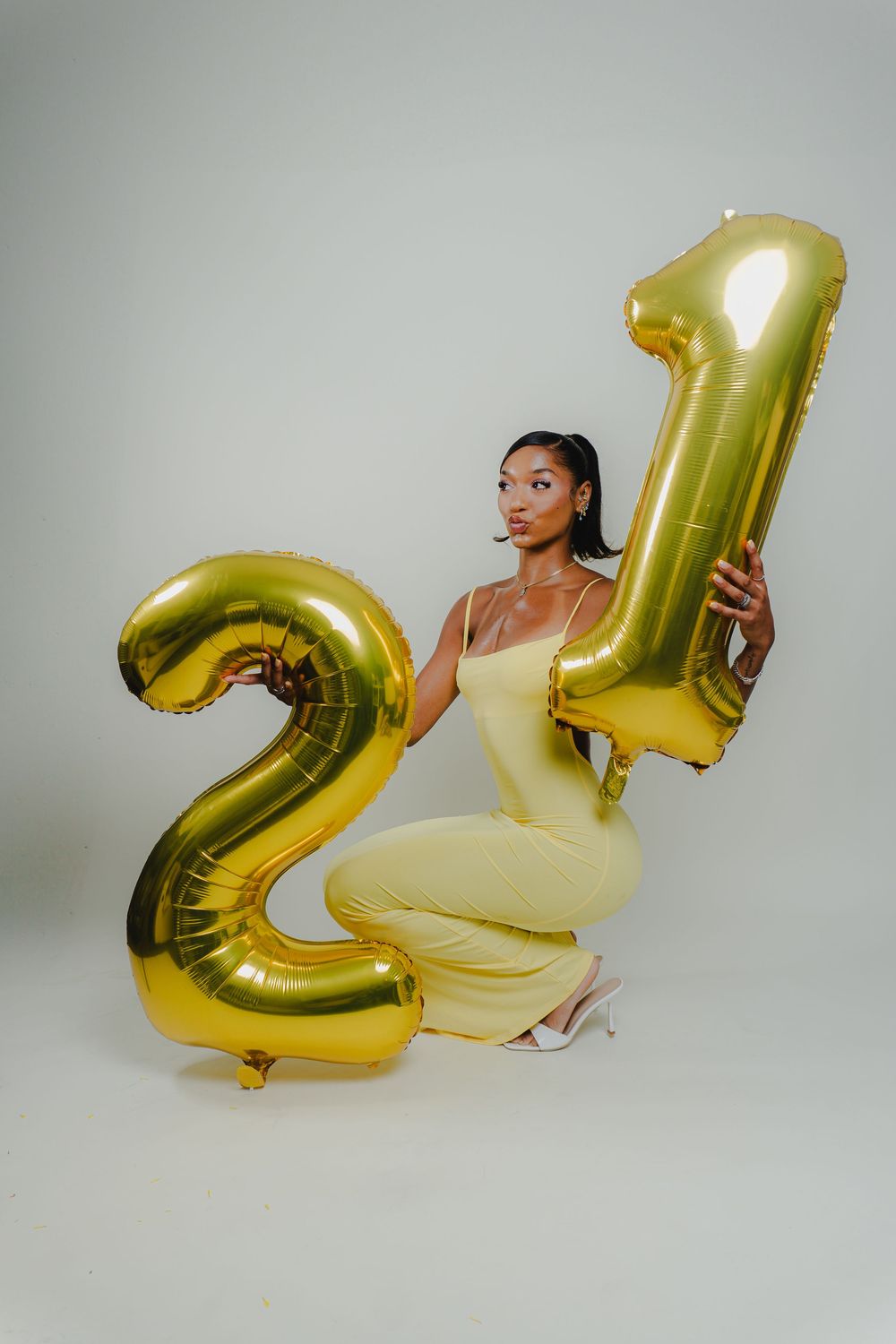 Birthday celebration shoot with gold number balloon and yellow dress against studio backdrop.