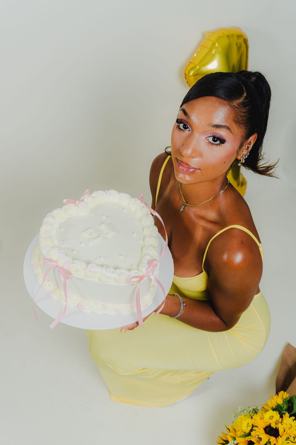Celebratory portrait with white heart-shaped cake and yellow dress for special occasion.
