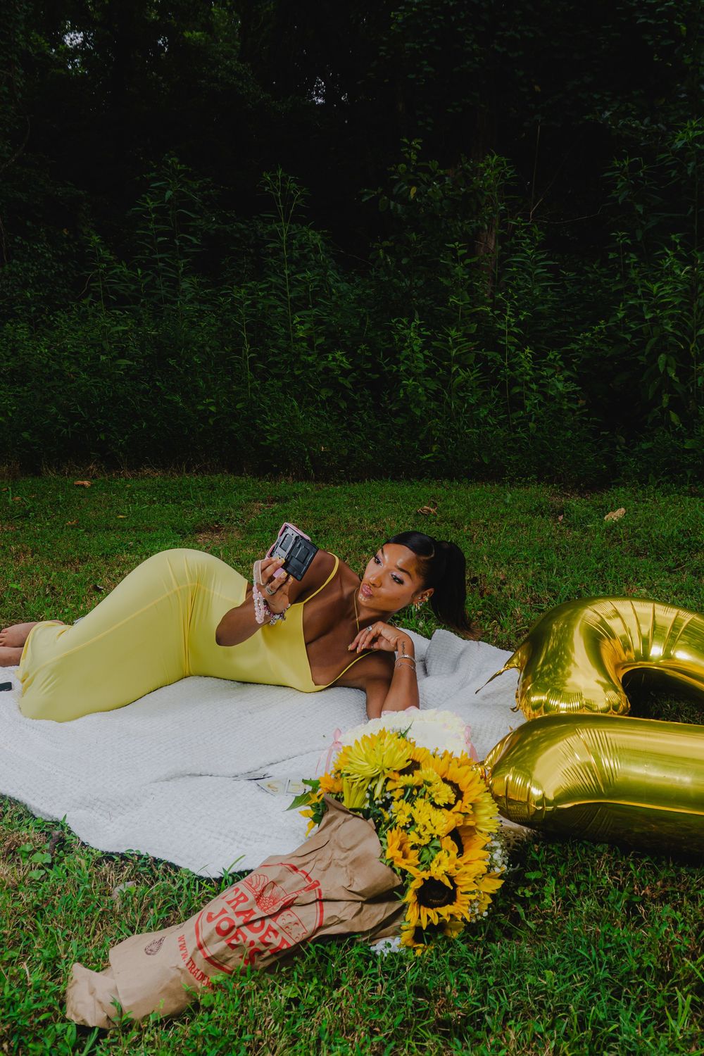 Outdoor portrait session featuring yellow dress and sunflowers arranged on white fabric against green foliage.