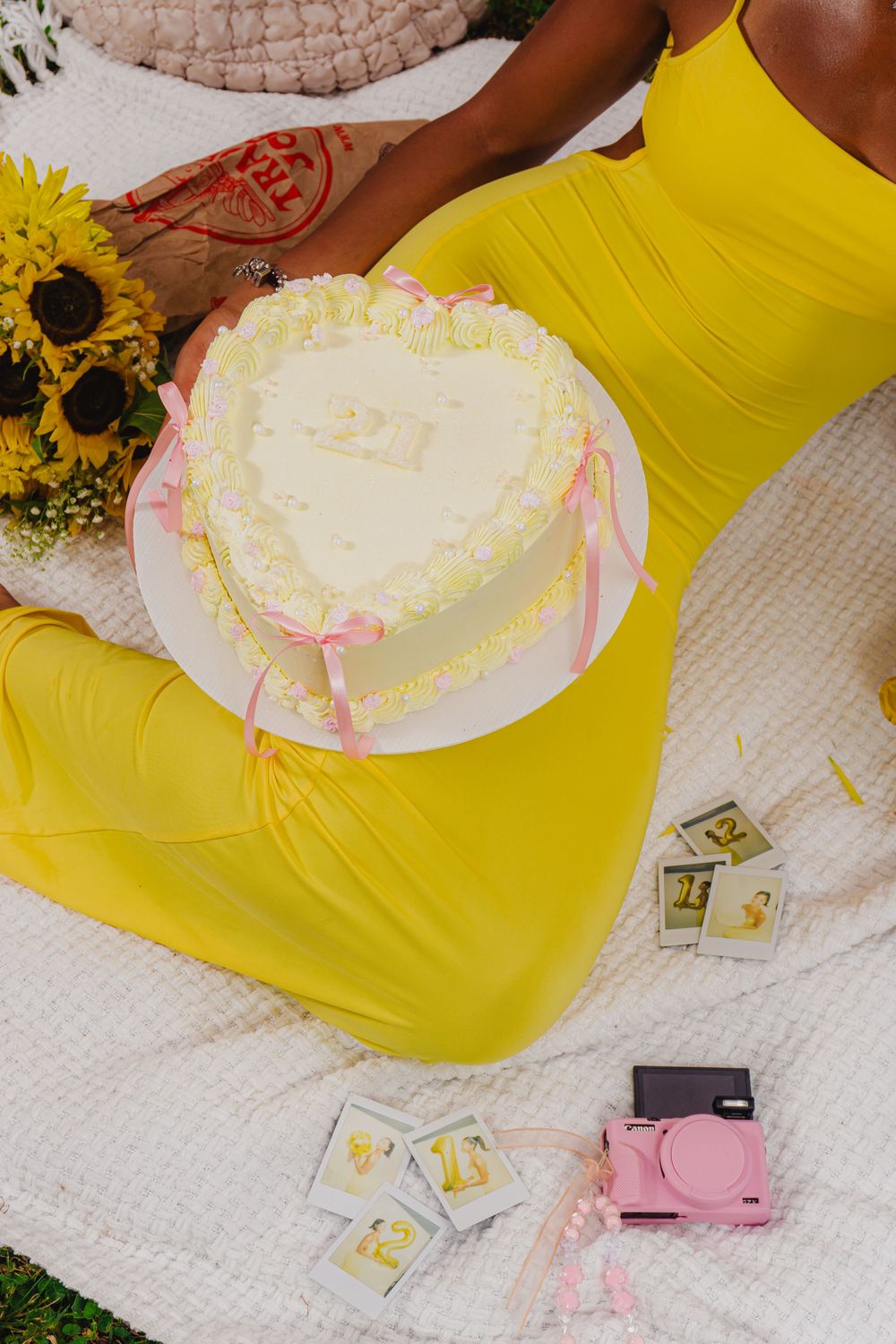 Close-up of white heart-shaped cake with pink ribbons next to yellow fabric and scattered decorations.