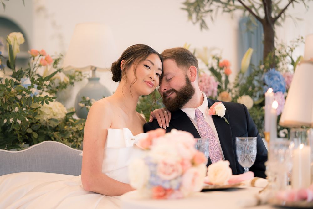 Bride and groom share an intimate moment at their wedding reception table surrounded by lush floral arrangements.