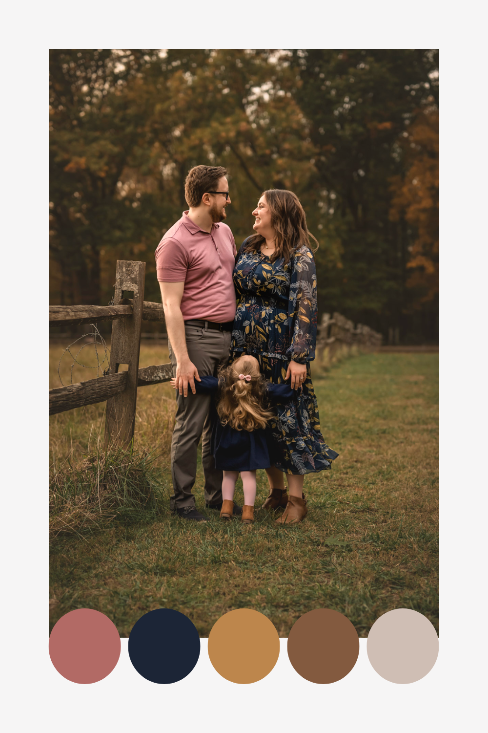 A family poses together by a wooden fence in an autumn field, wearing coordinated pink and floral outfits.