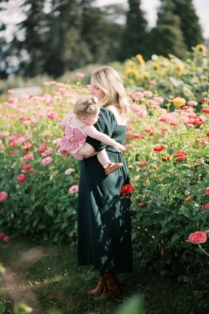 A tender moment captured in a garden of pink zinnias and sunflowers as a long green dress flows in the summer breeze.