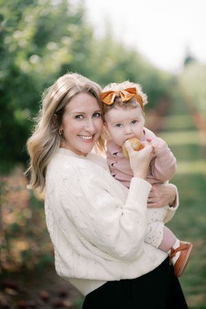 A tender autumn moment shared between parent and baby in an apple orchard wearing cozy cream sweaters.