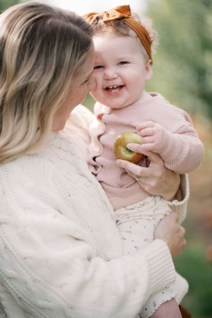 Tender family moment captured during autumn picnic with soft white sweaters and rustic outdoor setting.