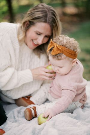 Cozy outdoor scene on white blanket showing loving interaction while sharing a pear in natural lighting.