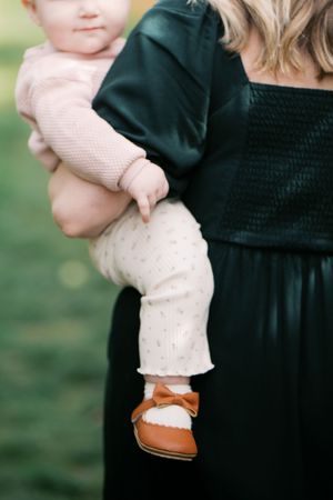 Close-up detail of tiny brown leather shoes and cream knit leggings against a dark dress.