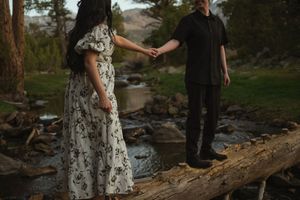 Lesbian couple holding hands and walking across a log during engagement photos in the Utah mountains
