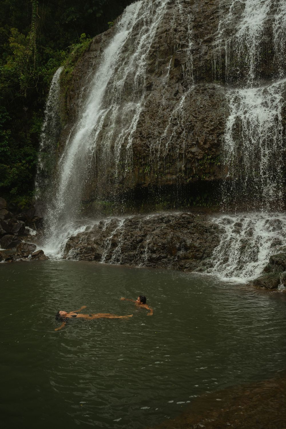 Couple swimming beneath a Kauai waterfall captured by a travel photographer