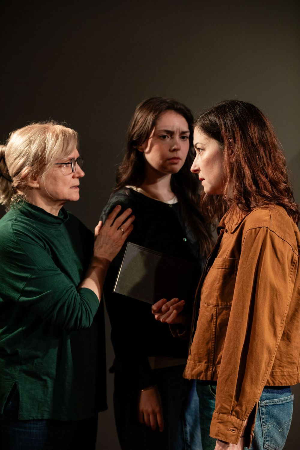 Three people engaged in an intense dramatic scene against a dark background.