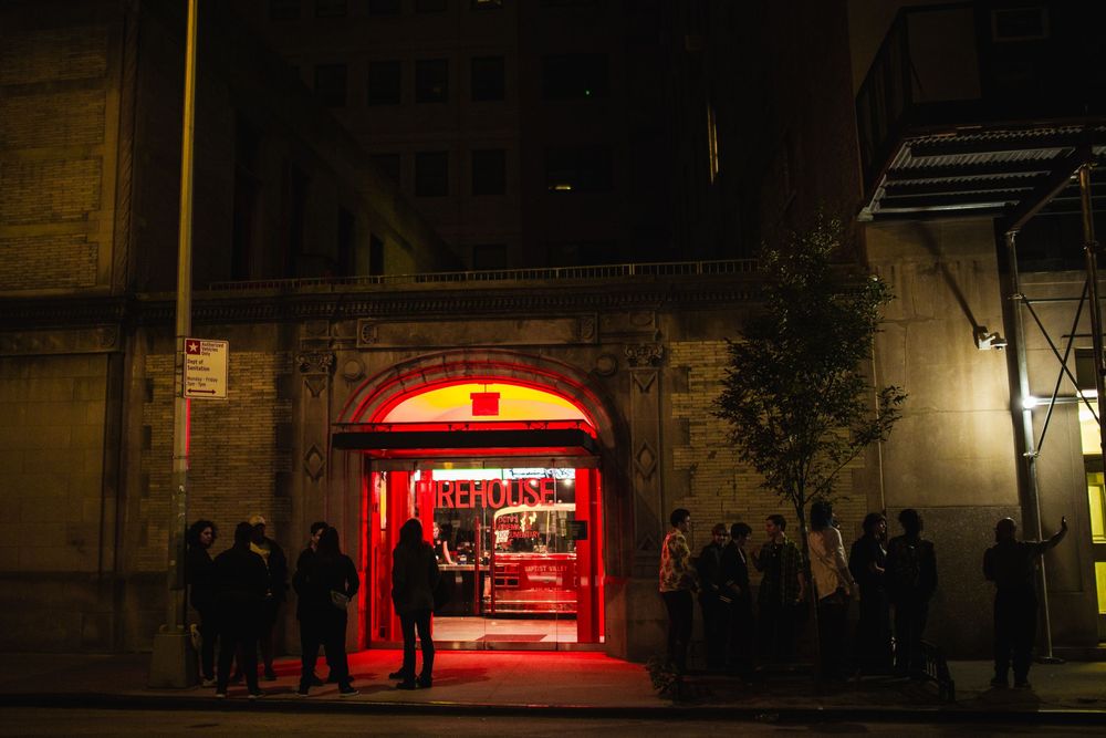 A red-lit entrance archway with people gathering outside at night.