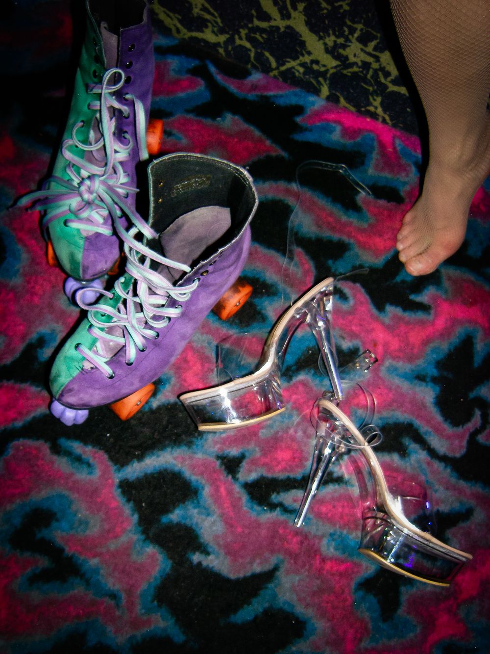 Purple roller skate and silver platform heel on colorful patterned carpet.