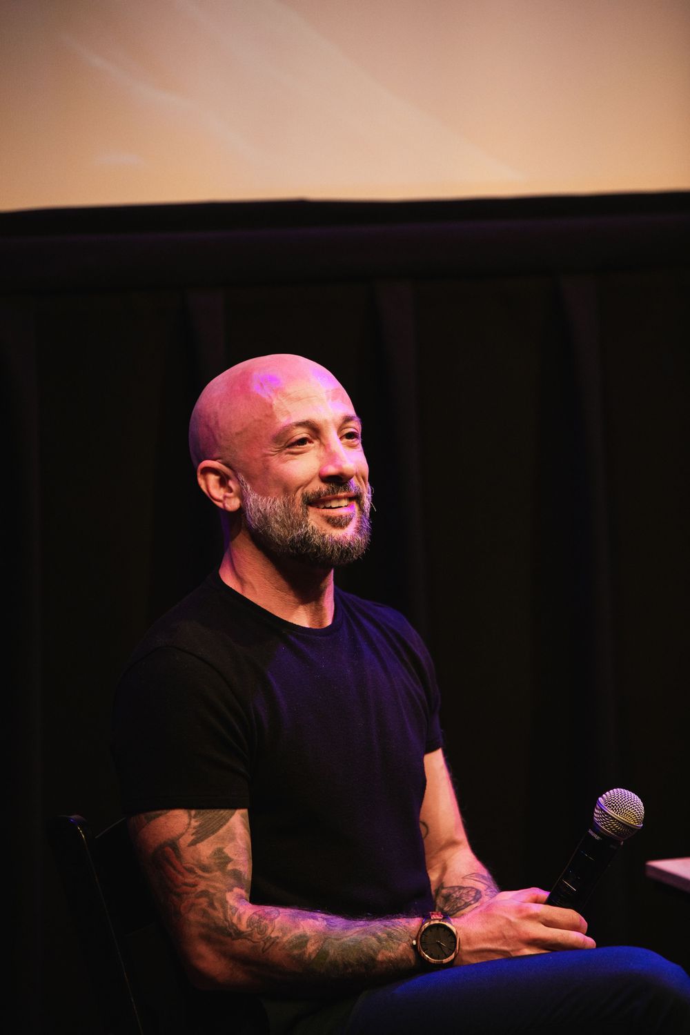 A speaker sits on stage illuminated by warm lighting during a presentation.
