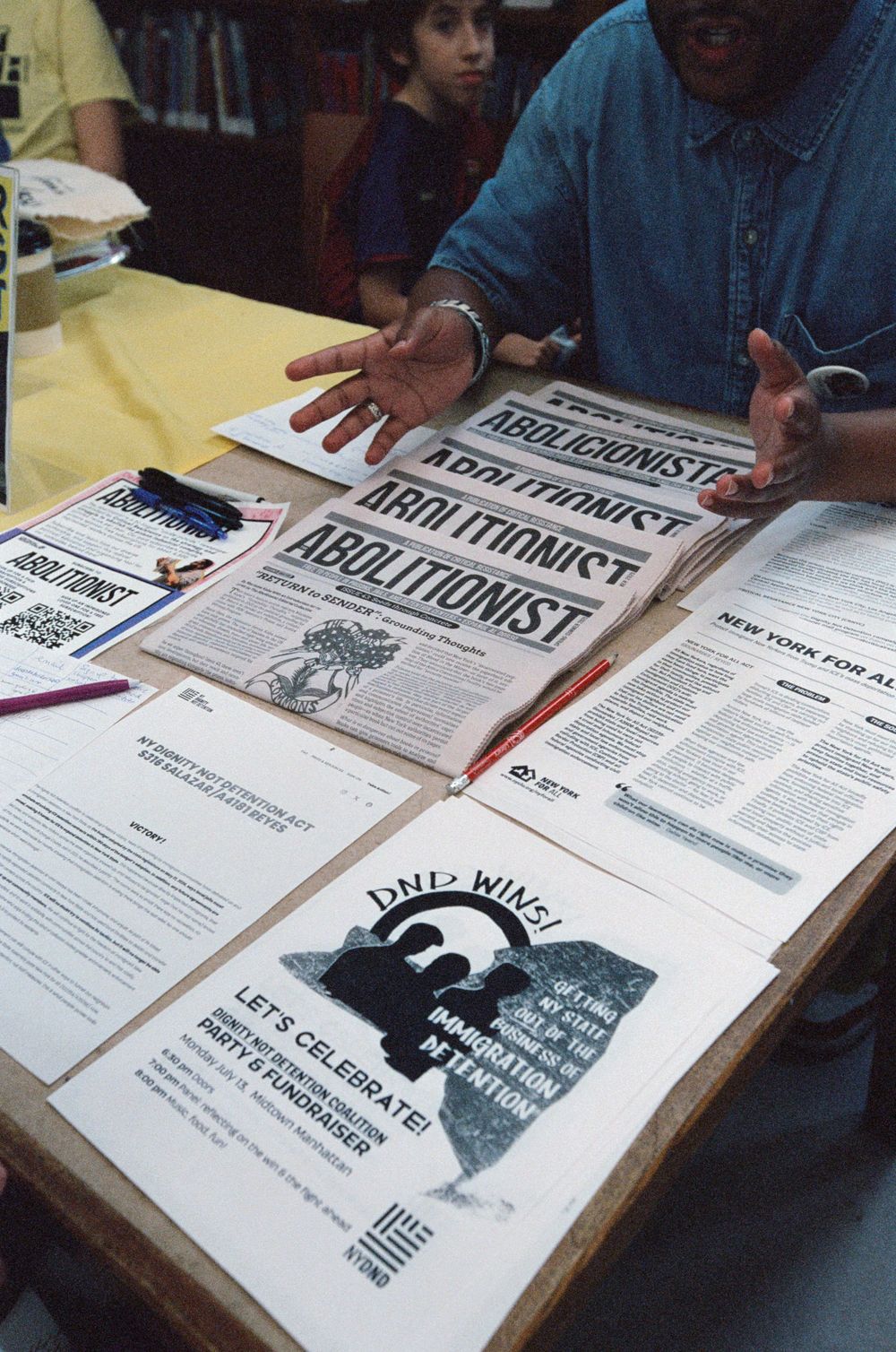 Person presenting Abolitionist newspapers and DND WINS flyers on a table at an activist gathering.