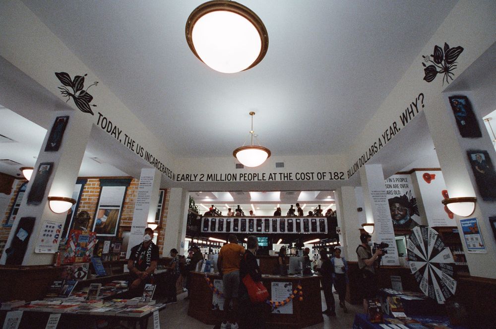 Interior of a busy store with white walls featuring bold text murals and pendant lights illuminating shoppers below.
