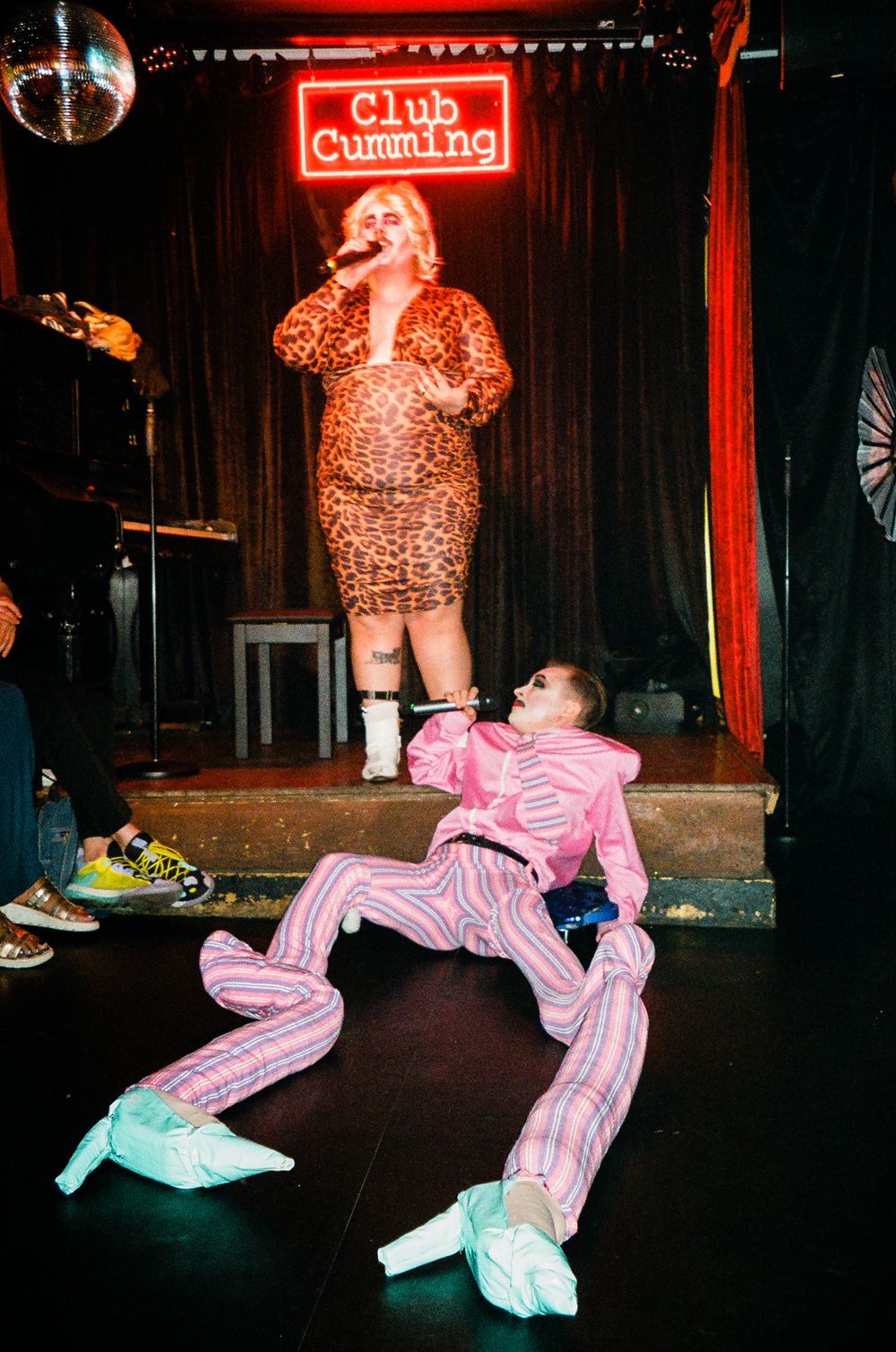 Drag performance at Club Cumming featuring performers in sequined outfits and pink clothing.