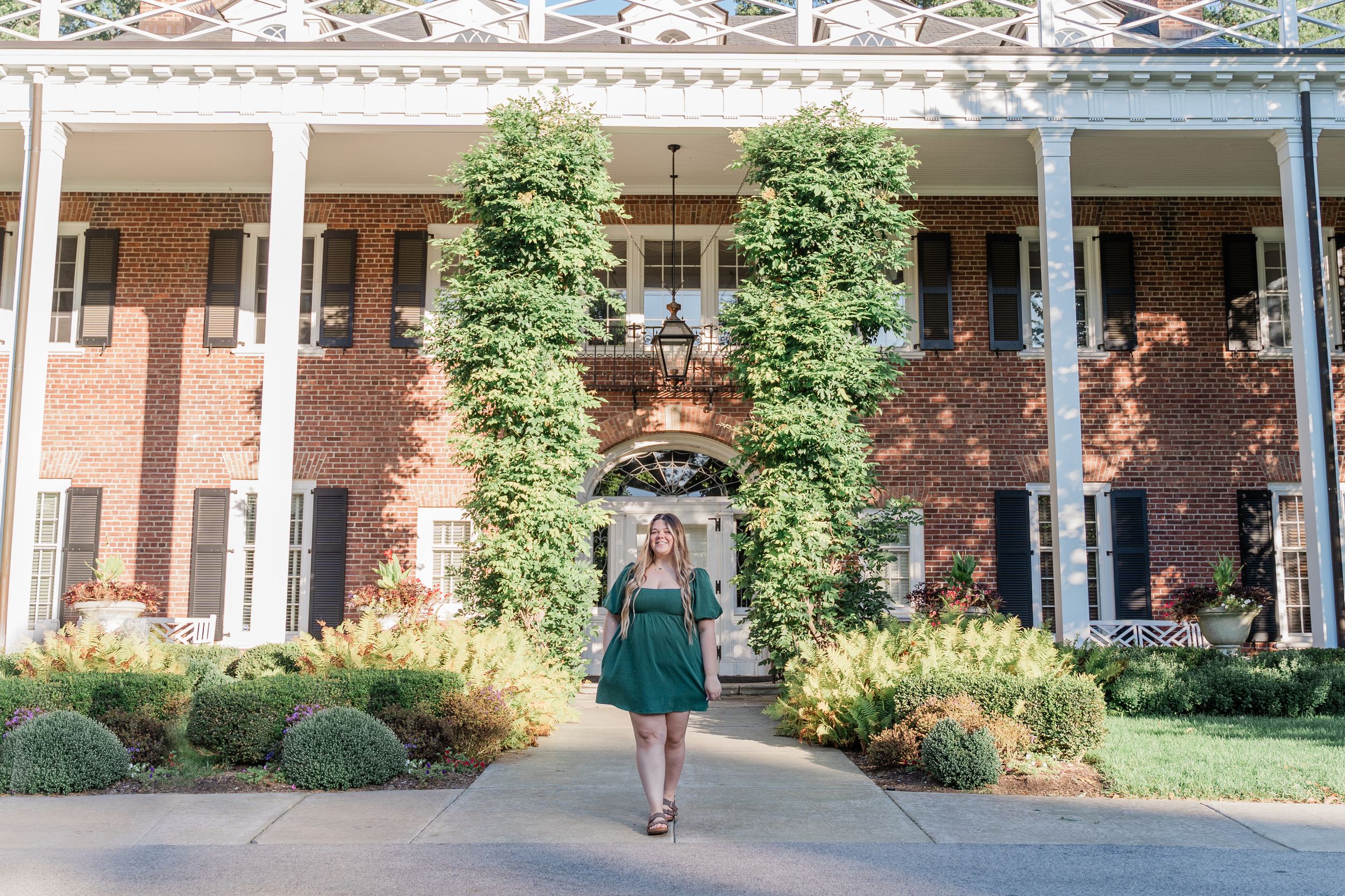 College students walk across a sunny campus courtyard with brick buildings and green landscaping in the background.
