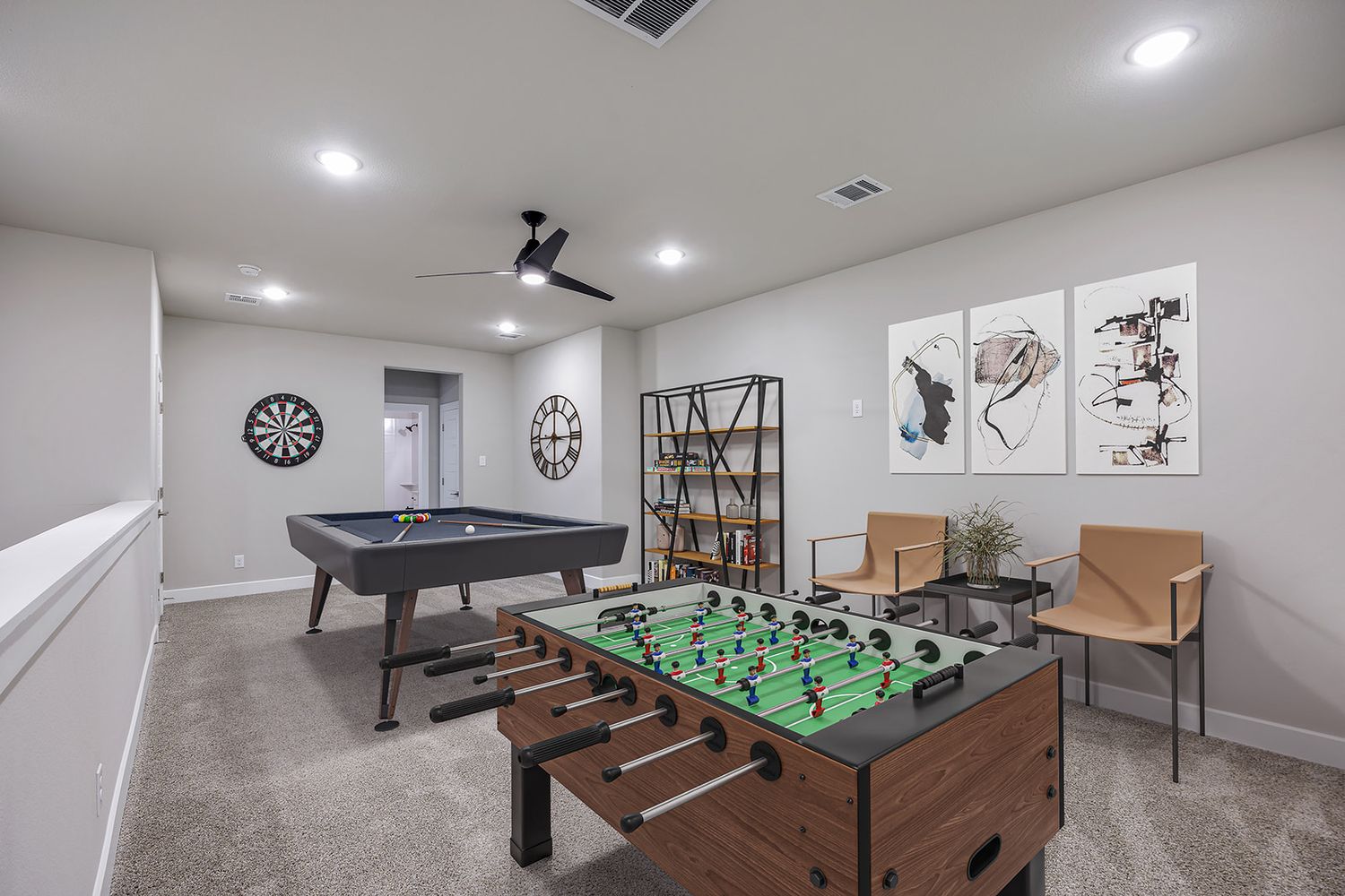 A spacious game room with multiple entertainment options including foosball, dart board, and table games in a bright interior.