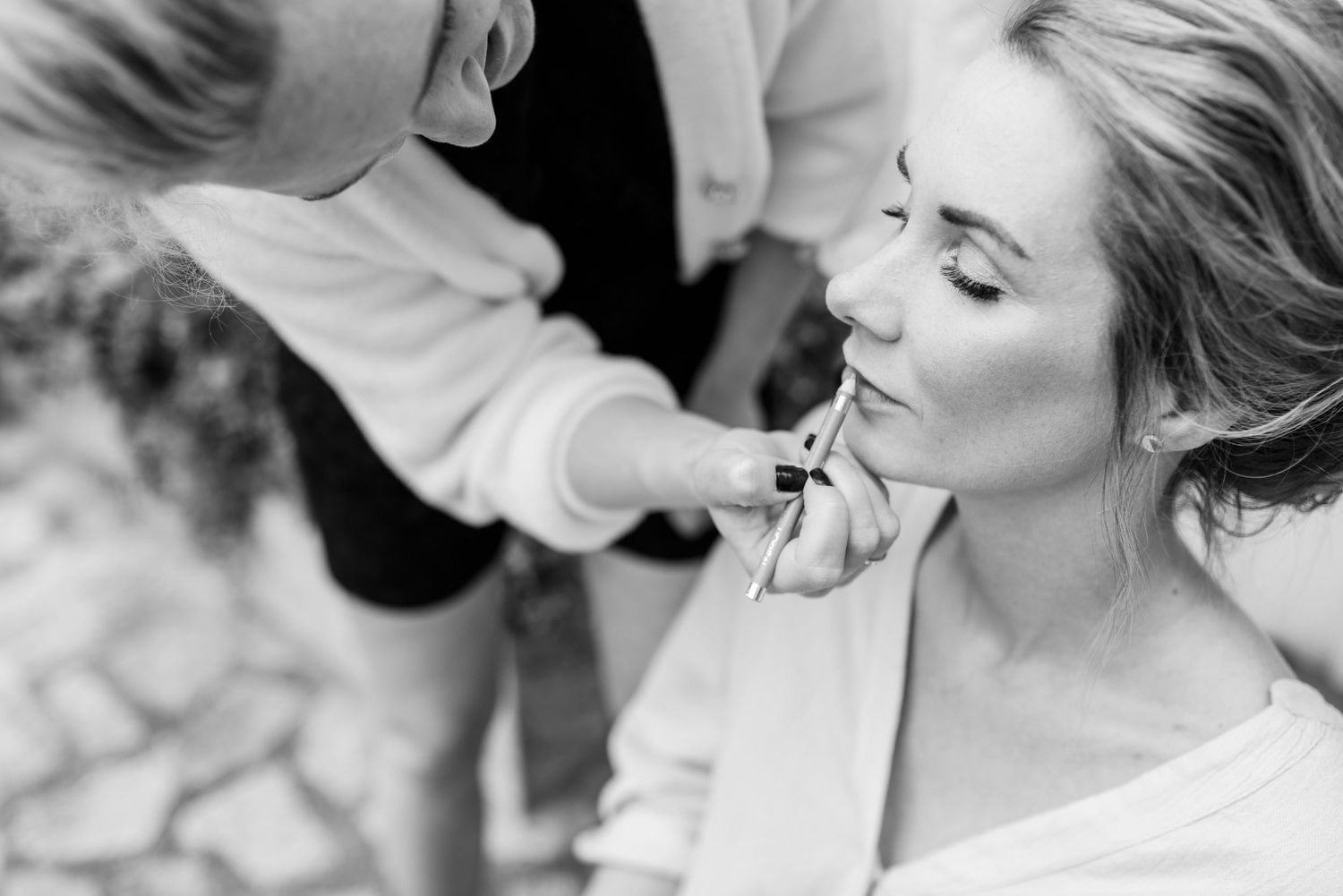 Schwarz-Weiß-Nahaufnahmen, einer Braut, die ihre Lippen geschminkt bekommt von der Stylistin, La Chia. In einem mallorquinischen Innenhof.