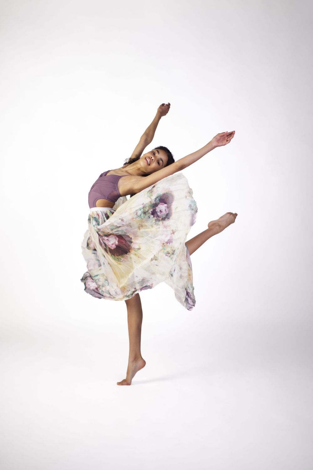 Dancer in flowing floral dress performs graceful arabesque poses against white background in three sequential shots.