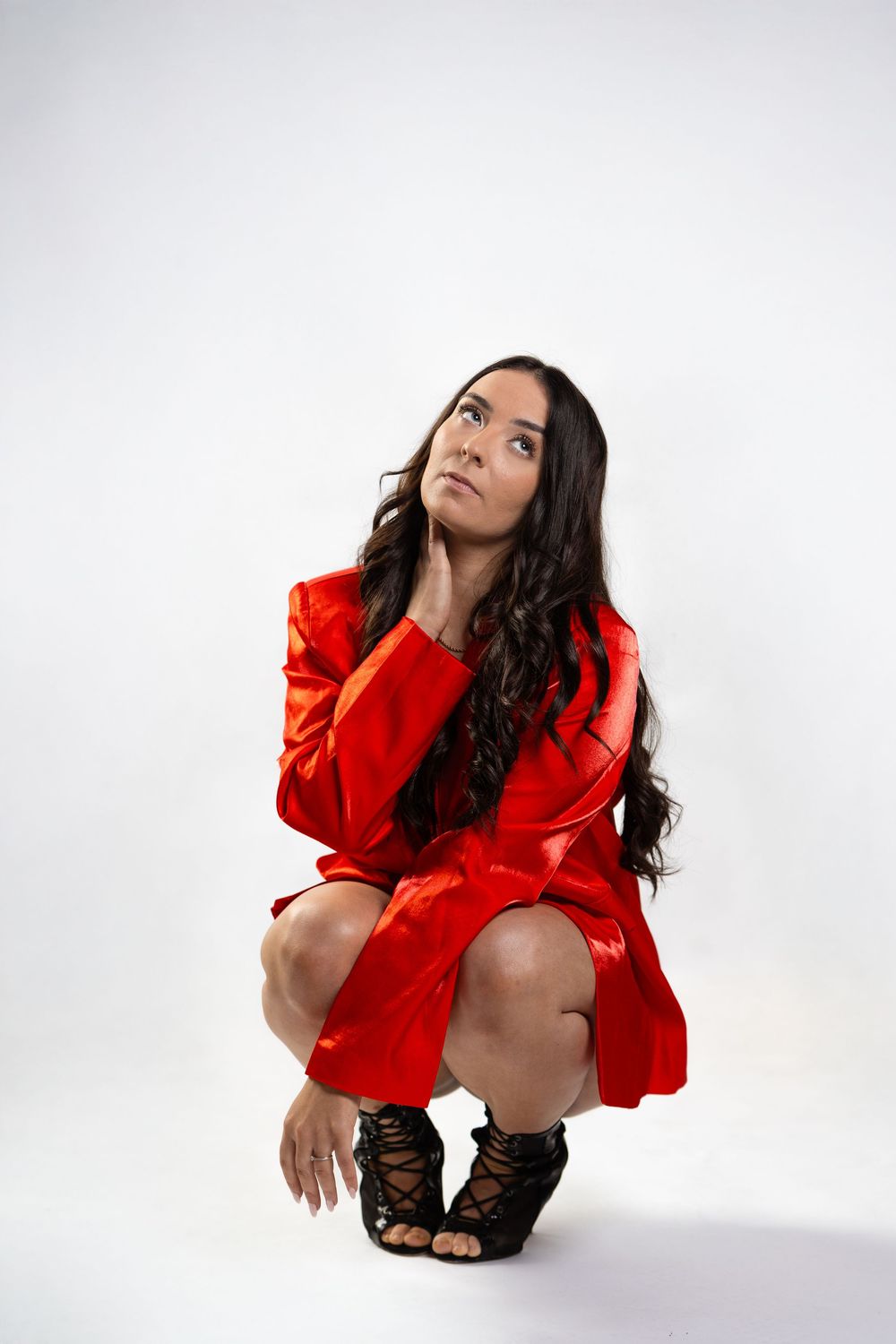 Fashion model in bright red blouse poses expressively in artistic studio portrait series against white background.