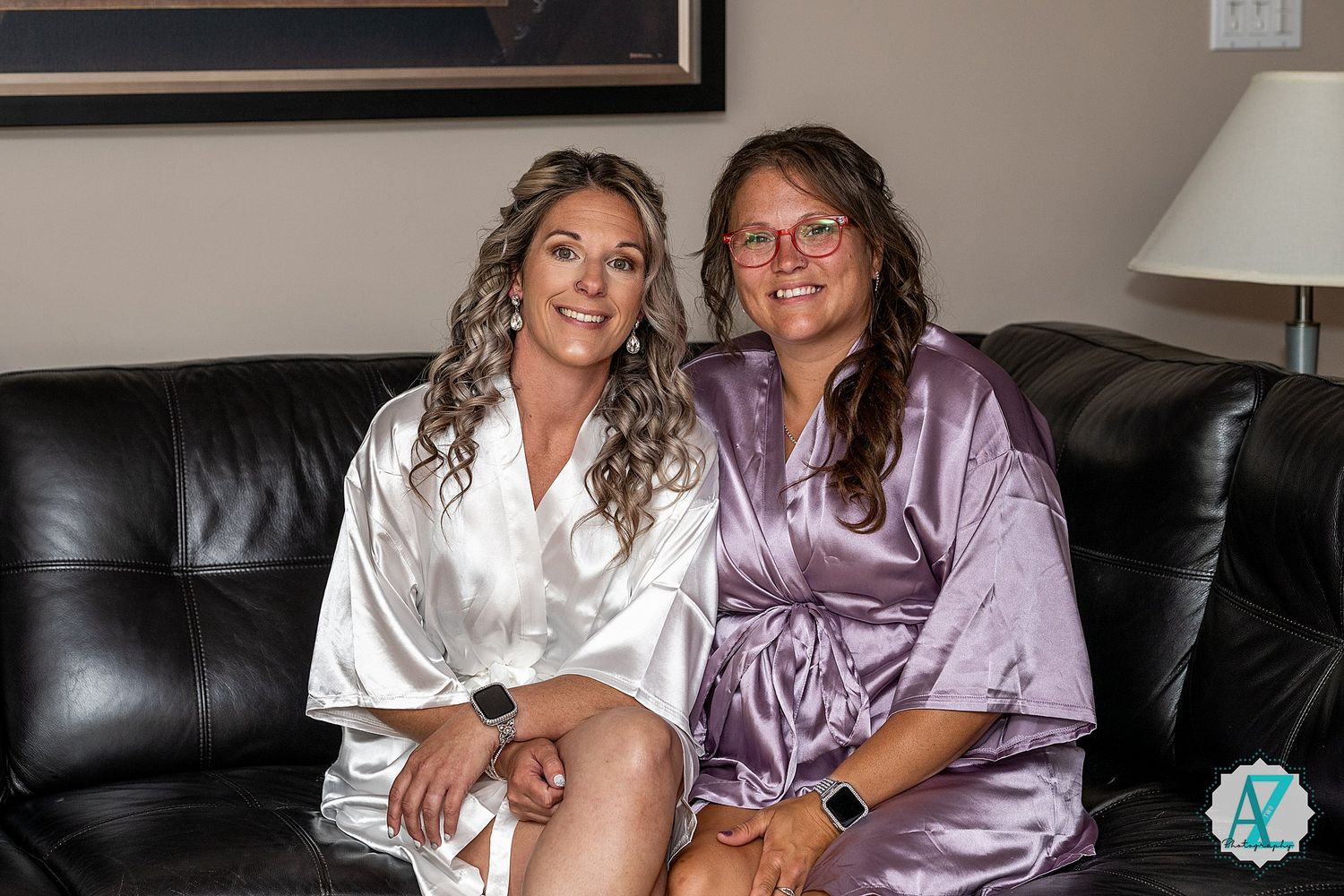 Two people in silk robes, one white and one purple, sit together on a black leather couch.