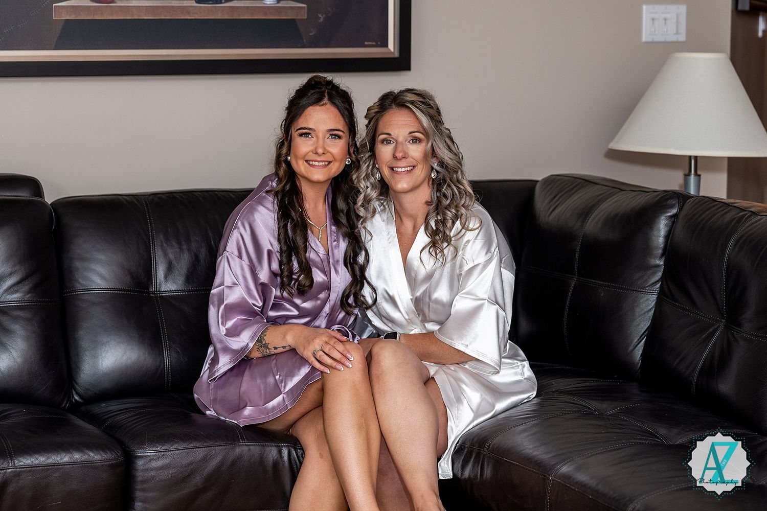 Two figures in silky robes smile together while sitting on a black leather couch.