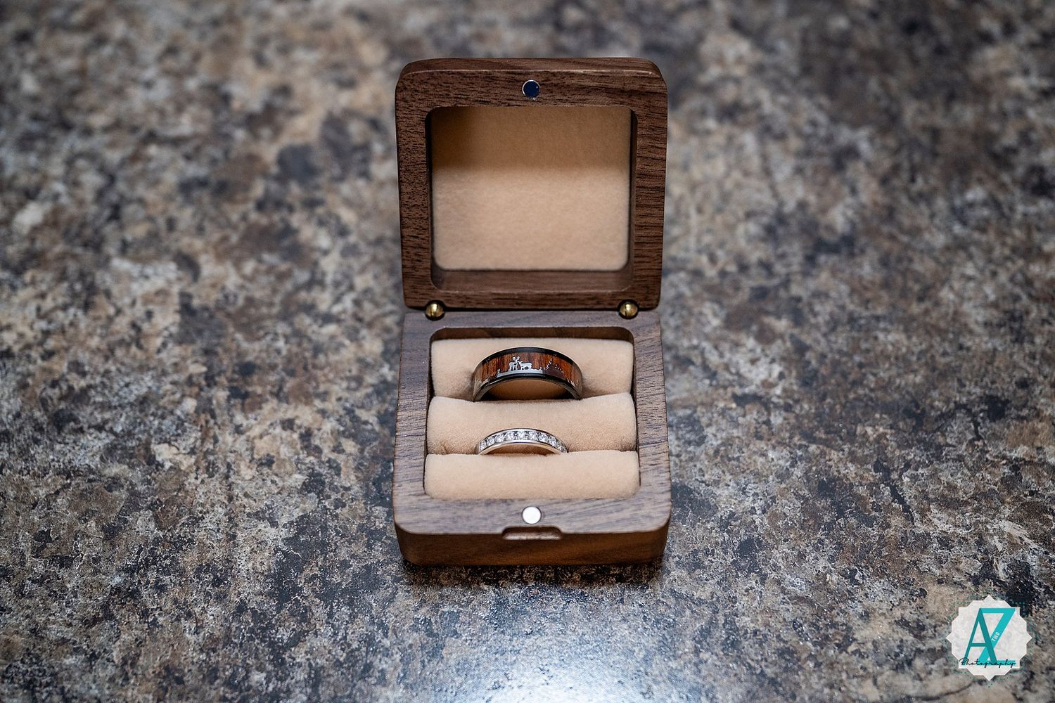 Wedding rings nestled in a small wooden box with light padding displayed on a textured stone surface.