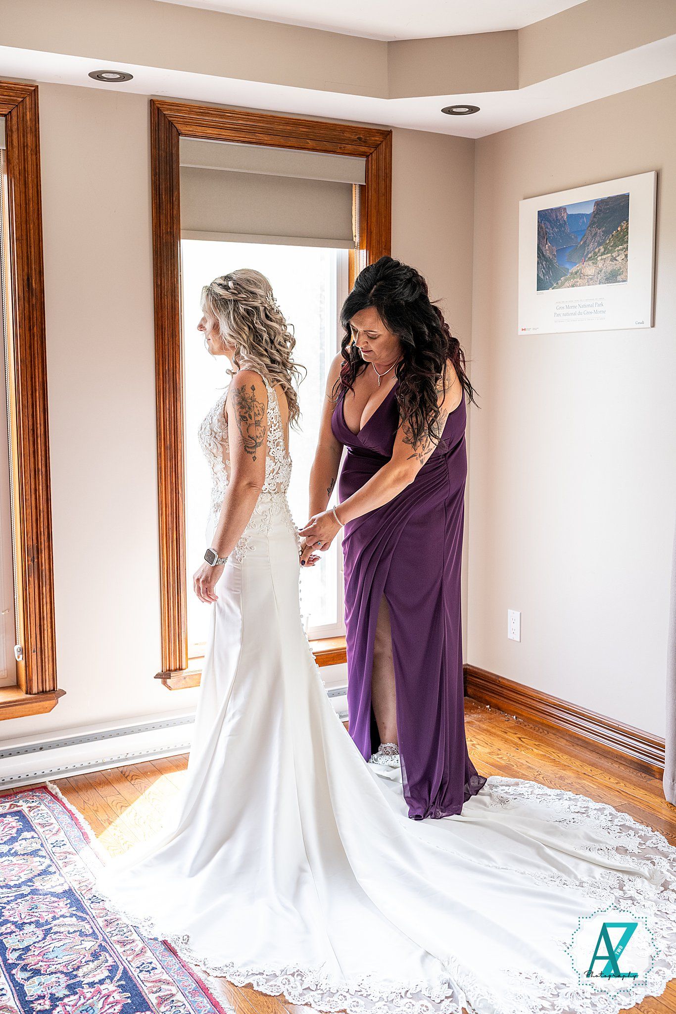 A wedding dress being adjusted and styled in a sunlit room with wooden trim and a decorative rug.