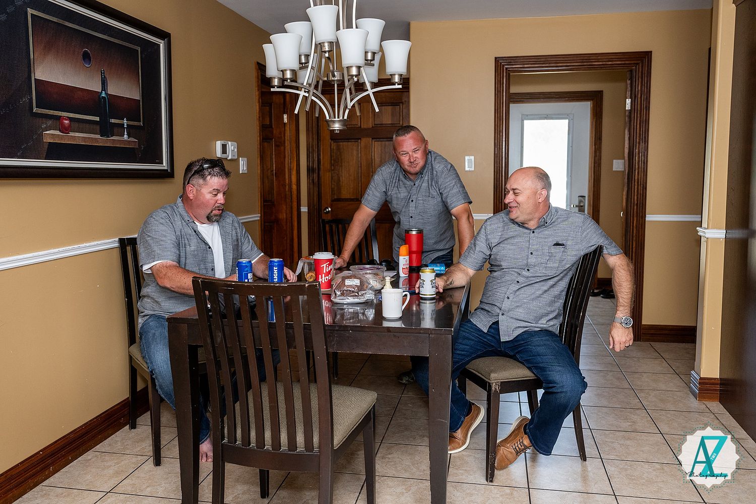Three people sit around a dining table under a chandelier in a room with tan walls.