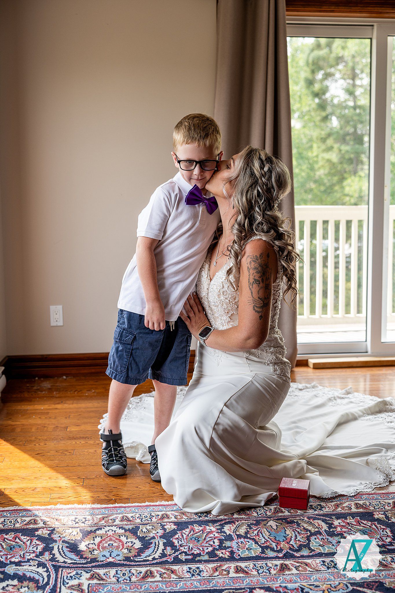 A tender moment between people in a bride's white gown and purple bow tie on hardwood floors with natural light.