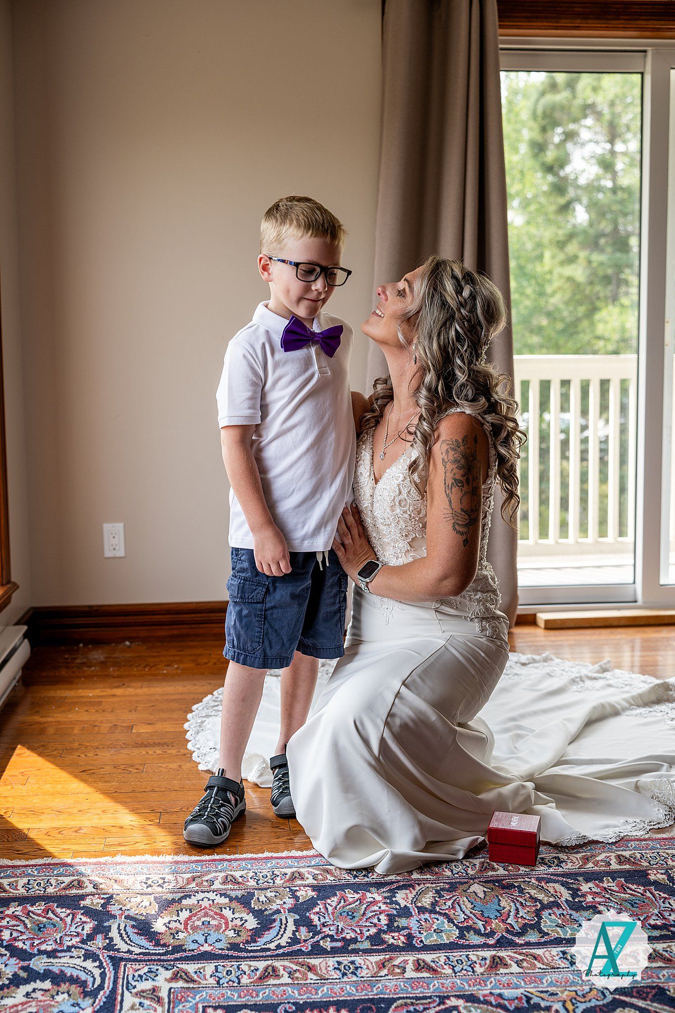 A sweet moment shared between a young boy in a bow tie and white polo shirt and a bride in a white gown on a Persian rug.