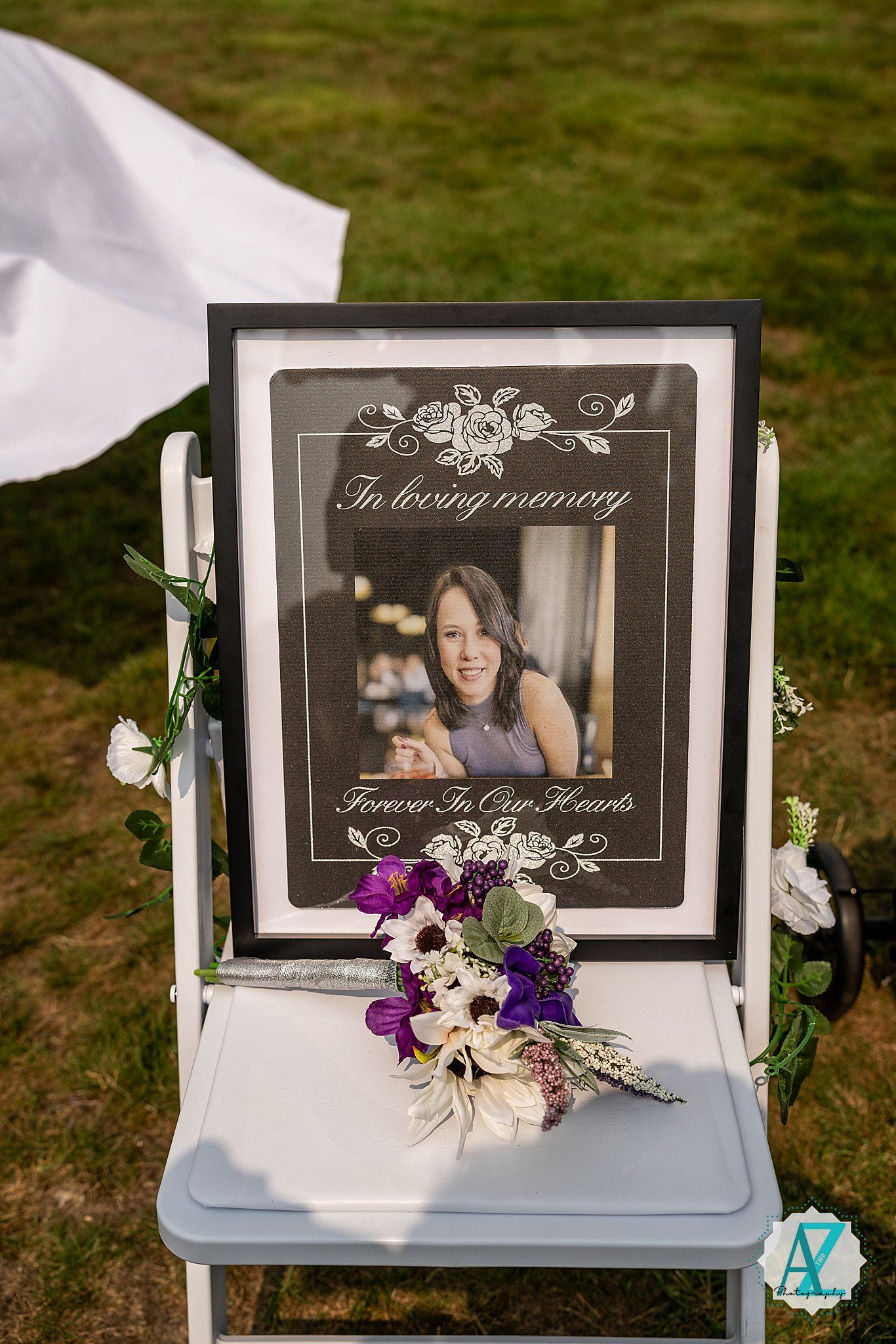 A framed memorial photo displayed on a white chair with purple and white floral decorations.