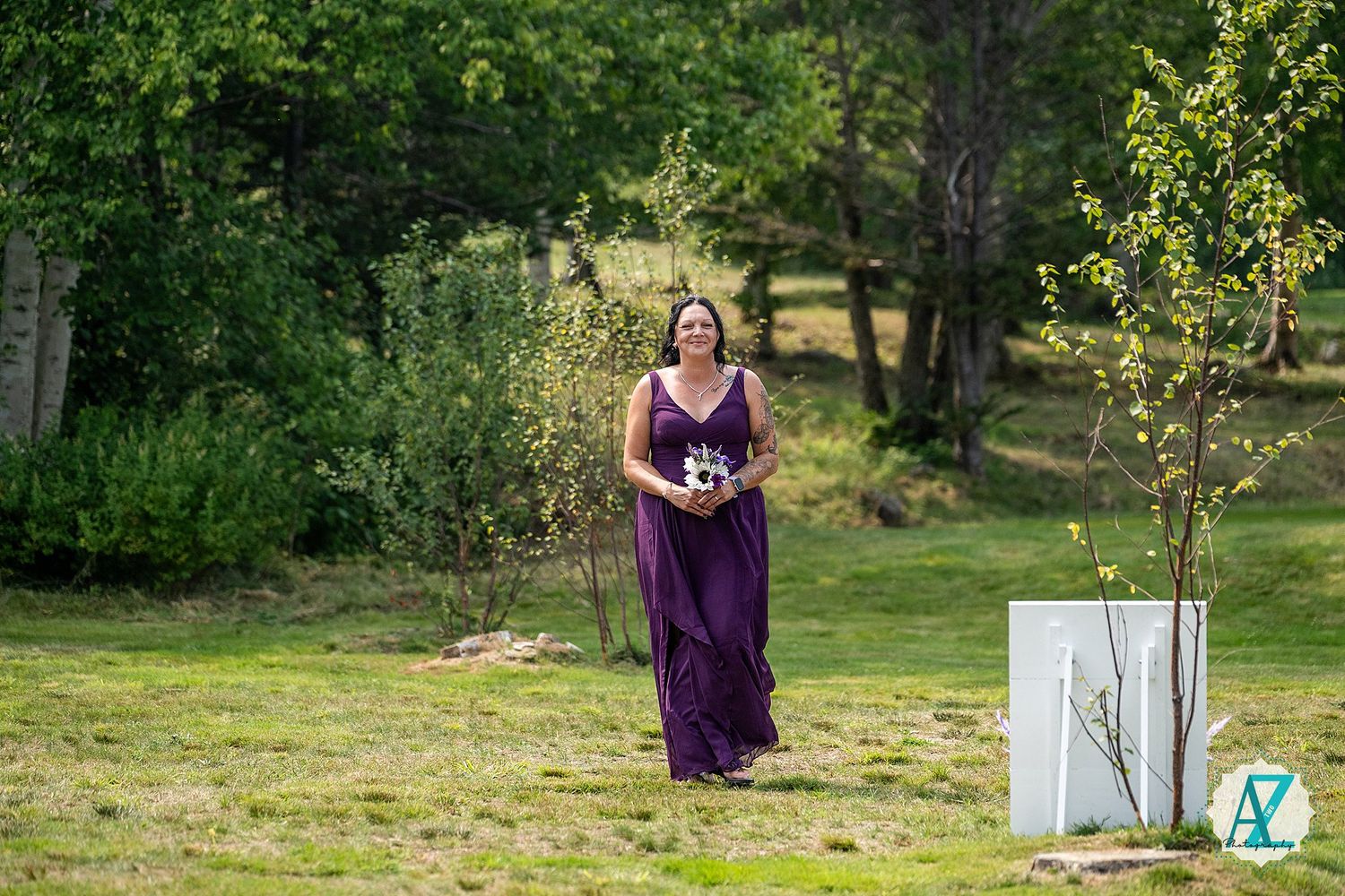 A person in an elegant purple bridesmaid dress walks across a sunny garden lawn during an outdoor ceremony.