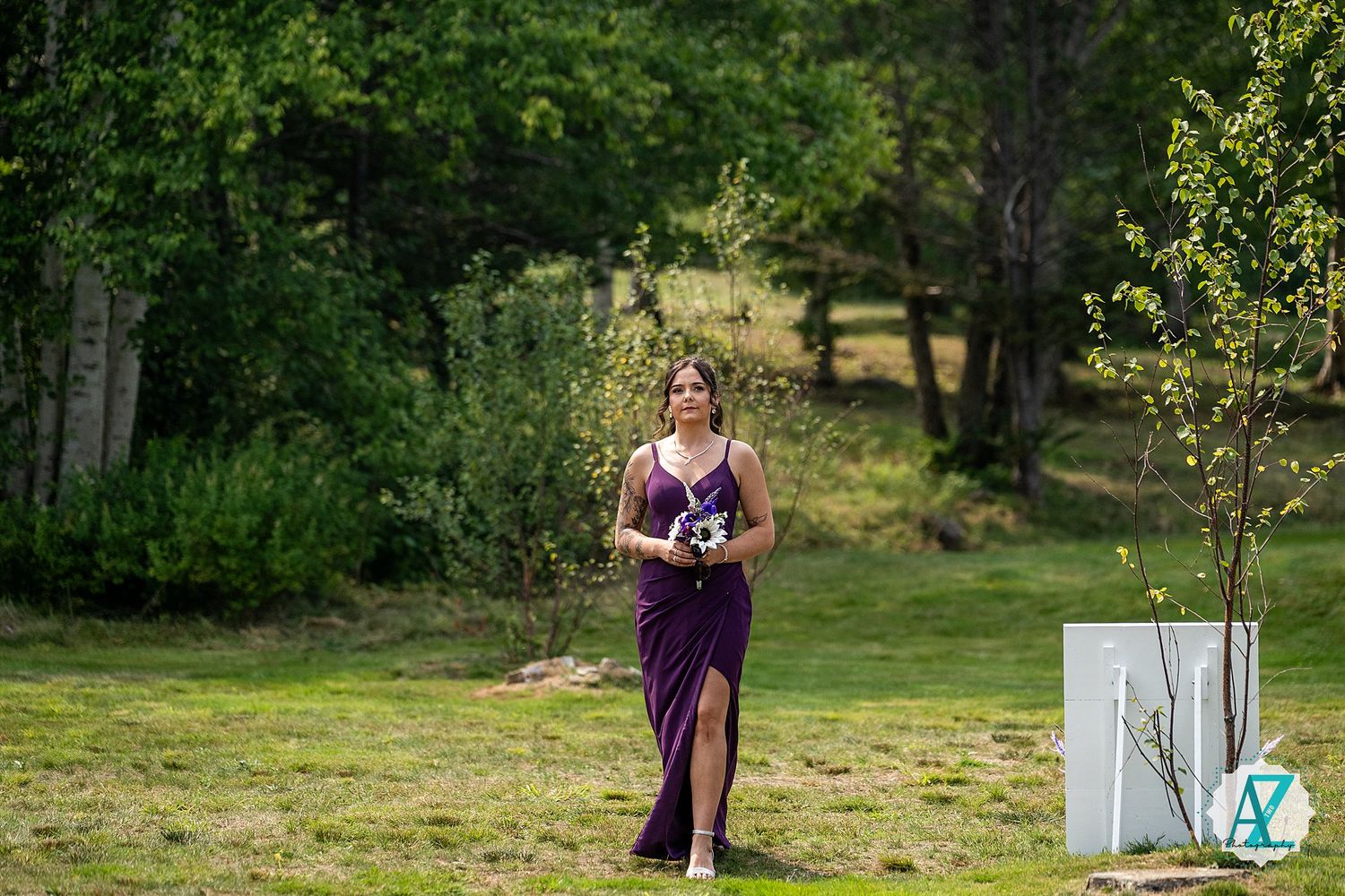A person in a long purple dress walks across a grassy lawn during an outdoor event.